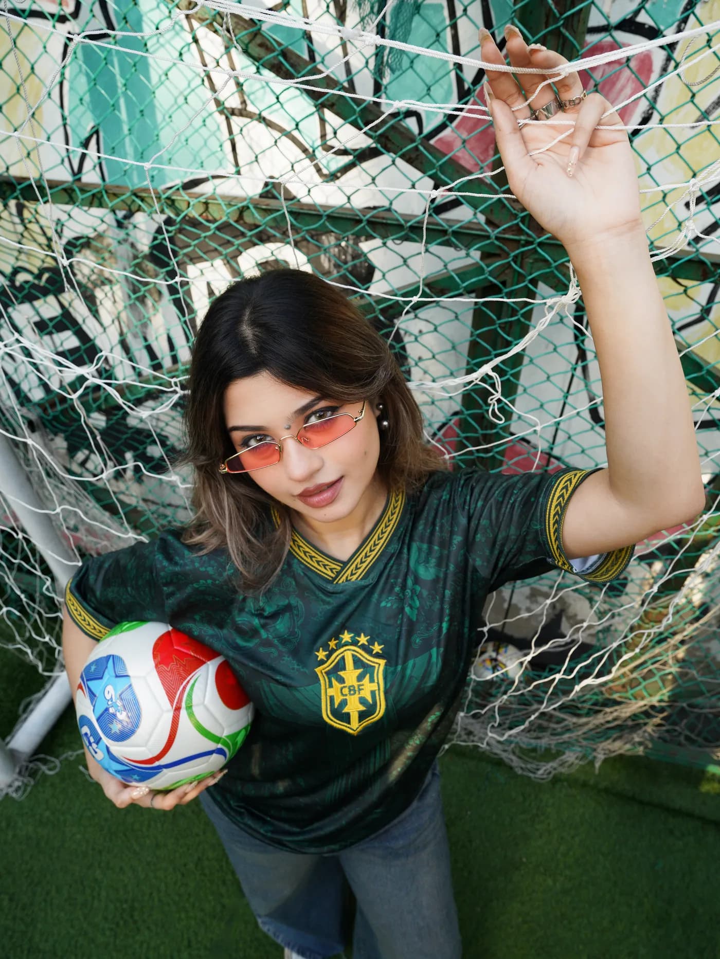 Model in the Verde jersey holding a ball inside a goal net